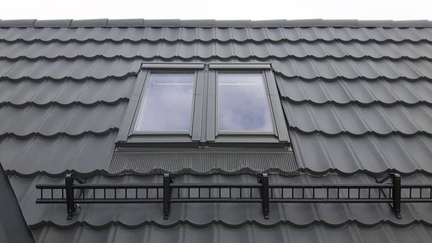 Et tak av svarte, bølgete takplater og taksikring med et nytt installert takvindu 