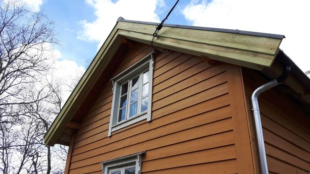En oransje hytte med vindu med hvite detaljerte vinduskarmer 
