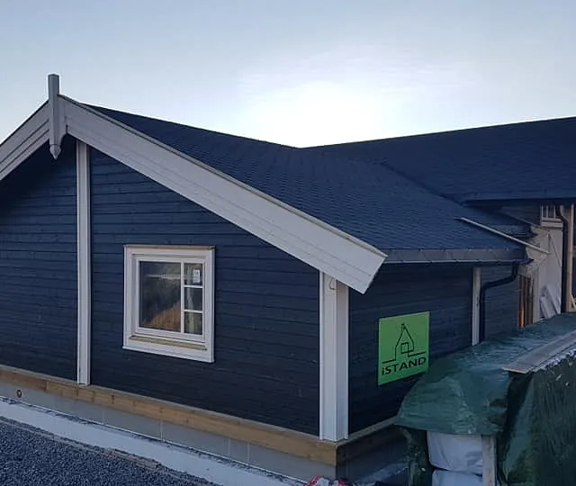 En ferdig bygt hytte i et hytte felt med hvite detaljer på hytten på vinduskarmer, inngangsdør, hytte hjørner og en utsikt over fjord og fjell