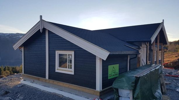 En ferdig bygt hytte i et hytte felt med hvite detaljer på hytten på vinduskarmer, inngangsdør, hytte hjørner og en utsikt over fjord og fjell