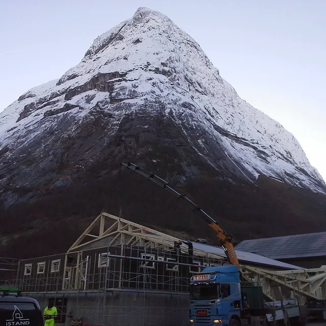 En kranbil legger tak på et bygg med et stort snekledd fjell i bakgrunnen