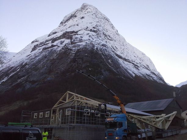 En kranbil legger tak på et bygg med et stort snekledd fjell i bakgrunnen