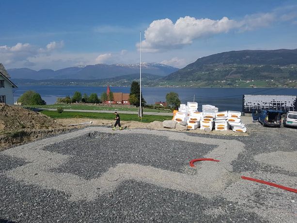 Oppstart betongarbeid med en ansatt i bakgrunnen med en haug med oppgravd jord på ene siden og masse utstyr til det nye huset på høyre siden ved siden av to firmabiler