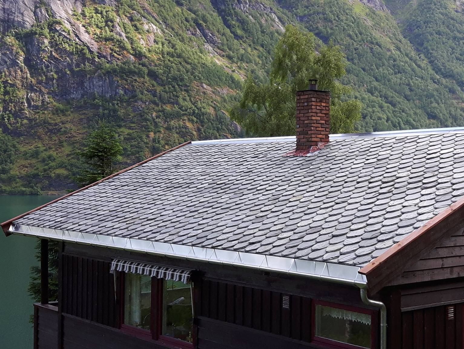 Nytt skifertak på et hus med to piper som stikker opp fra taket og en fjord i bakgrunnen