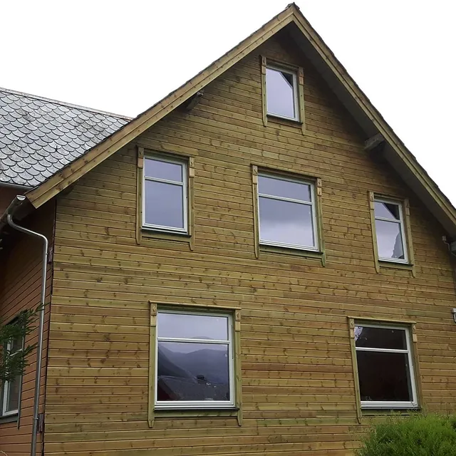 En hel side av et hus med skiftet vegg kledning og vinduer som ikke har blitt beiset enda og som har skifertak