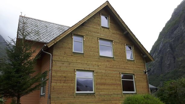 En hel side av et hus med skiftet vegg kledning og vinduer som ikke har blitt beiset enda og som har skifertak