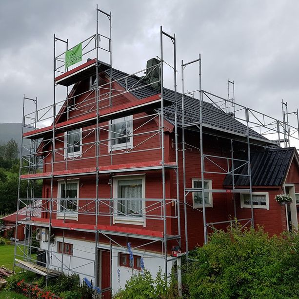 Stilas satt opp et rødt hus med iStand AS logo på for å bytte kledning og tak med en grå sky og fjell ibakgrunnen