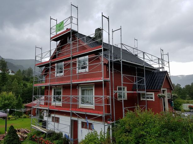 Stilas satt opp et rødt hus med iStand AS logo på for å bytte kledning og tak med en grå sky og fjell ibakgrunnen
