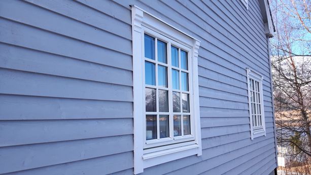 Hvite vindu på et grått hus med detaljer på vinduskarmene