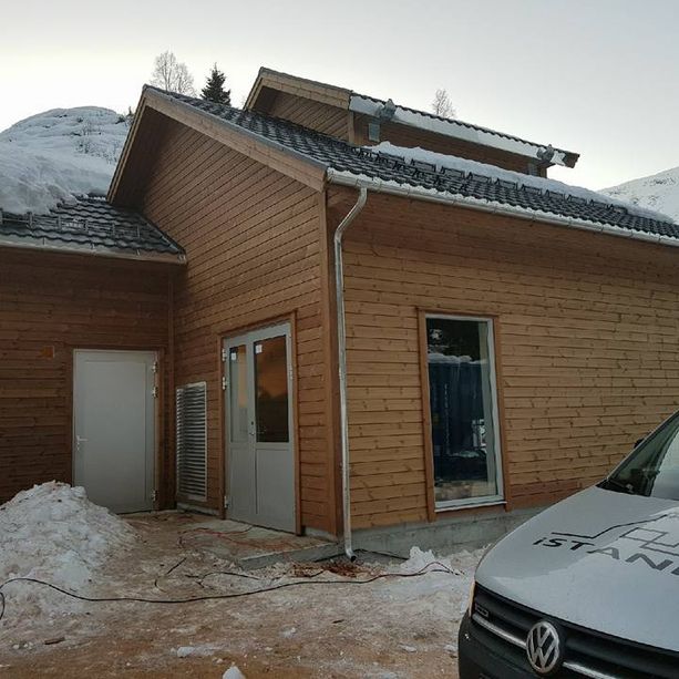 Et ferdig tilbygg på et hus med snø på takene, moderne vindu og en firmabil i forgrunnen