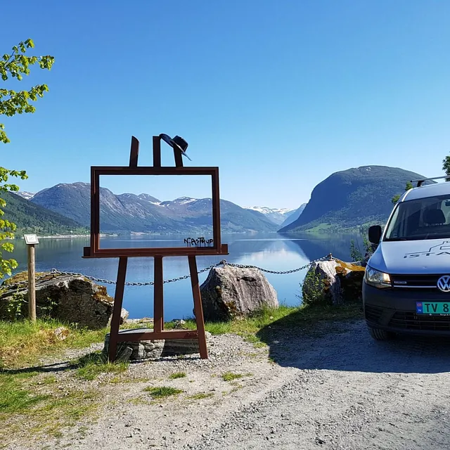 iStand AS firmabil som står ved siden av et kunst prosjekt med utsikt over fjord og fjell