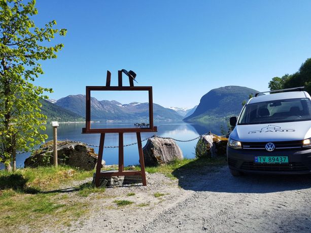 iStand AS firmabil som står ved siden av et kunst prosjekt med utsikt over fjord og fjell