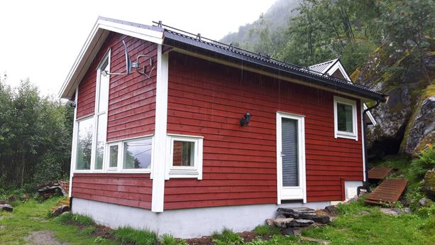 En rød hytte med noen store og noen små vindu med hvite vinduskarmer og en dør med en liten steintrapp