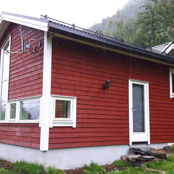 En rød hytte med noen store og noen små vindu med hvite vinduskarmer og en dør med en liten steintrapp