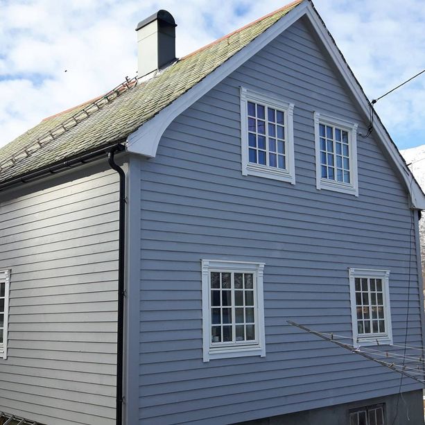 Grått hus med hvite vindu med detaljer på vinduskarmene og tak kant med en pipe som kommer opp fra taket