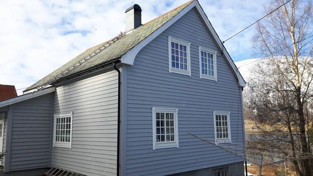 Grått hus med hvite vindu med detaljer på vinduskarmene og tak kant med en pipe som kommer opp fra taket