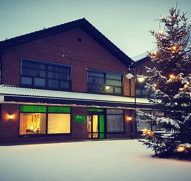 iStand AS sitt firmabygg med mange store vindu, firmalogo i vinduene og tak og bakke dekket i snø med et fjell i bakgrunnen samt et tent juletre i forgrunnen