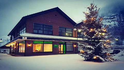 iStand AS sitt firmabygg med mange store vindu, firmalogo i vinduene og tak og bakke dekket i snø med et fjell i bakgrunnen samt et tent juletre i forgrunnen