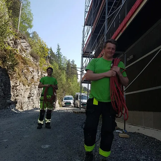 To ansatte som bærer ting inn i et hus som holder på å bli bygd opp