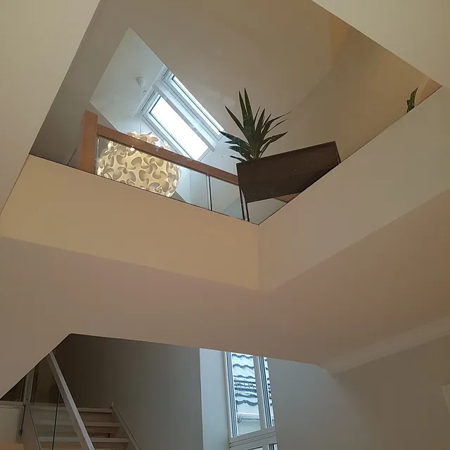 Et takvindu nærme trapper som gir folk i 1 etasje innsyn til 2 etasje hvor det står en stol og en plante
