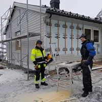 To ansatte som arbeider med etterisolering til et hus som har stilas satt opp rundt seg
