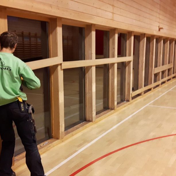 to ansatte som jobber med å fjerne planker fra ferdig installerte vinduer i en gymsal
