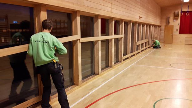 to ansatte som jobber med å fjerne planker fra ferdig installerte vinduer i en gymsal