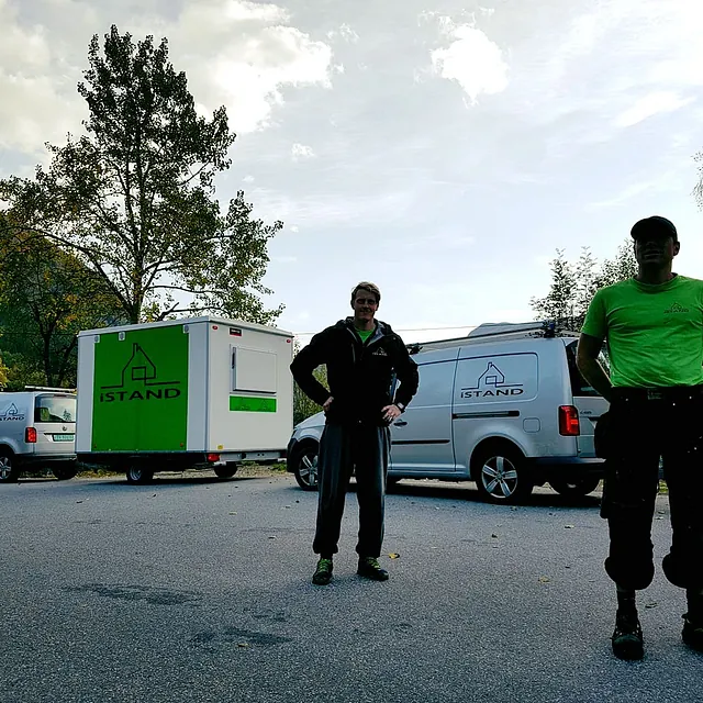 To ansatte som står foran firmabiler med tilhengere som har firma logoen på 