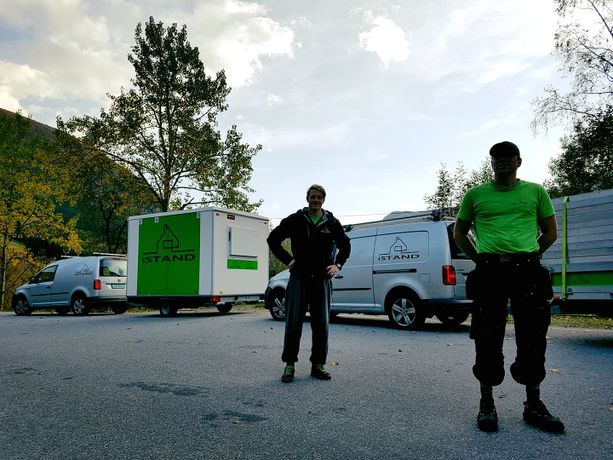 To ansatte som står foran firmabiler med tilhengere som har firma logoen på 