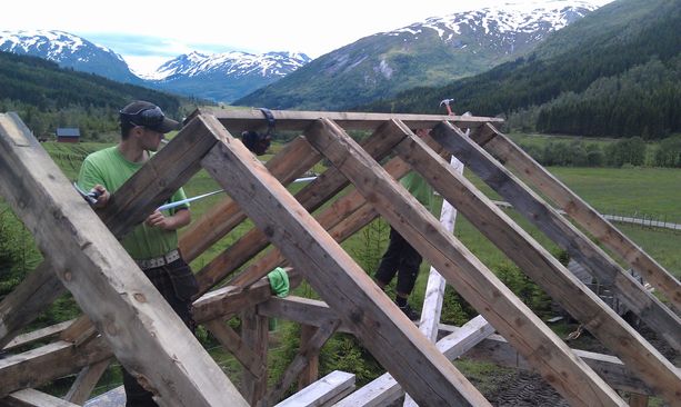 To ansatte som setter opp skjelettet til et hus i et lite bebodd område omringet av fjell 