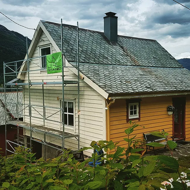Et stilas med firmalogo oppført på en side av et hus som skal rehabiliteres 