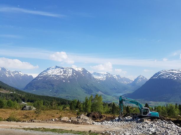en gravemaskin som graver ut en ny tomt med en utsikt av blå himmel, daler, fjell med snødekte fjelltopper