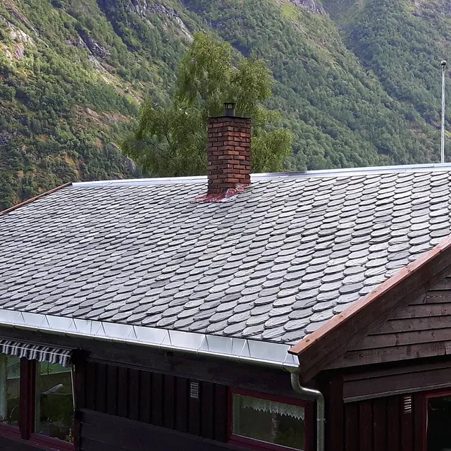Nytt skifertak på et hus med to piper som stikker opp fra taket og en fjord i bakgrunnen