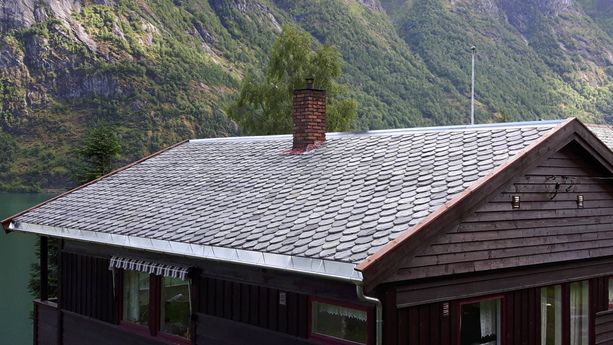 Nytt skifertak på et hus med to piper som stikker opp fra taket og en fjord i bakgrunnen