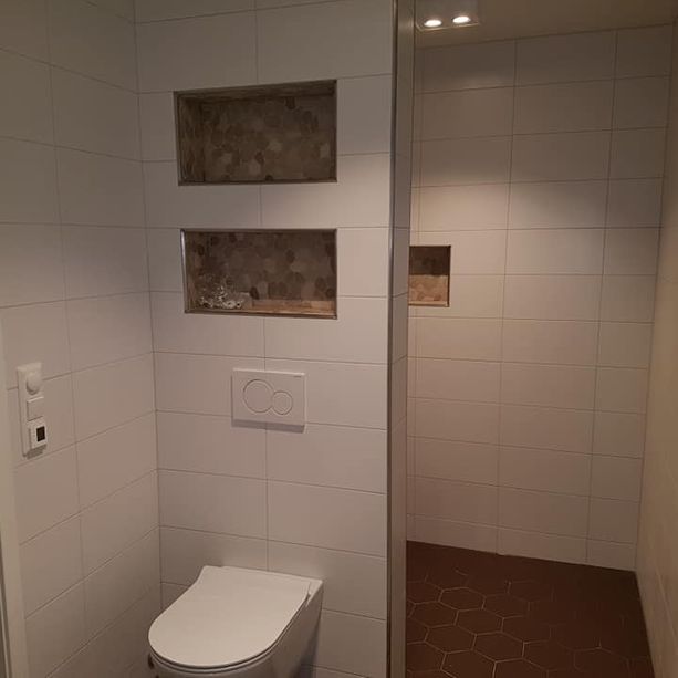 Lite bad med moderne toalett og spotlys i taket samt innebygde hyller over toilettet og i dusjen 