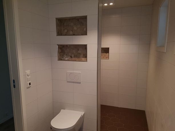 Lite bad med moderne toalett og spotlys i taket samt innebygde hyller over toilettet og i dusjen 