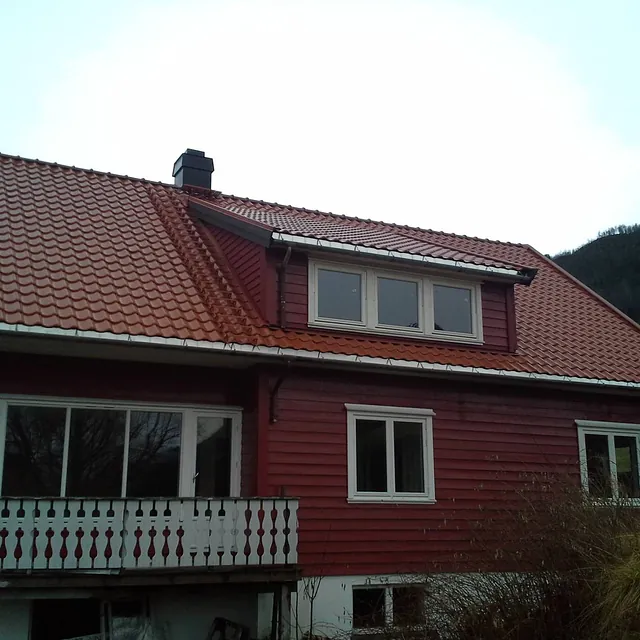 Et rødt hus med vinduer som har hvite detaljerte vinduskarmer og hvitt tradisjonelt gelender på balkongen hvor store enkle vinduer og en balkong dør leder ut til