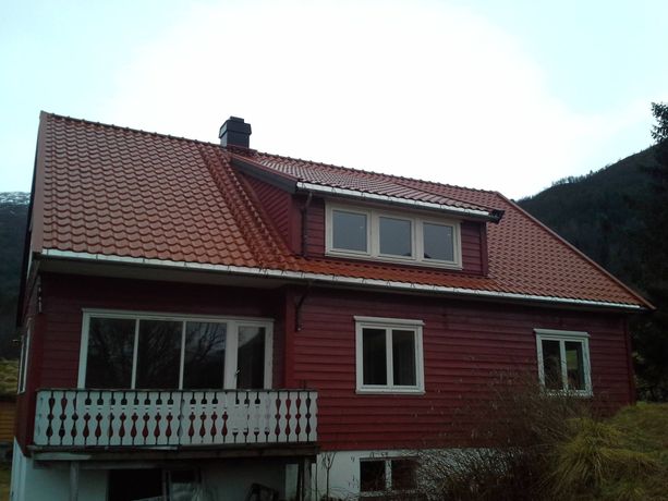 Et rødt hus med vinduer som har hvite detaljerte vinduskarmer og hvitt tradisjonelt gelender på balkongen hvor store enkle vinduer og en balkong dør leder ut til