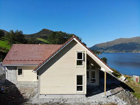 T formet hus med rødt tak og mange vindu med hvite vinduskarmer som har en utsikt ut over fjord og fjell