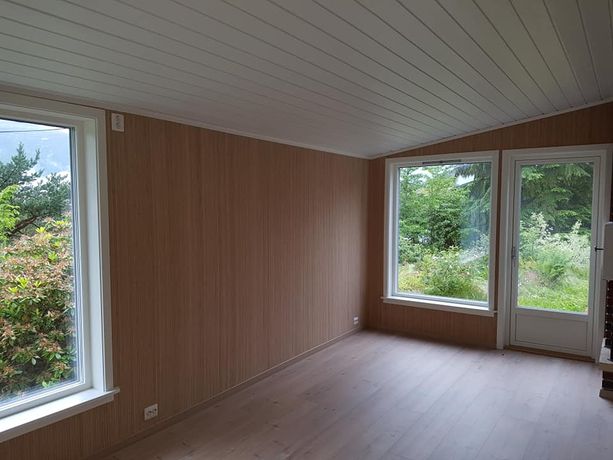 Innsiden av en stue med store vindu, hvitt tak og hvite vindu- og dørkarmer