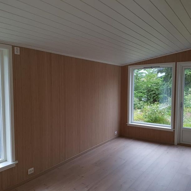 Innsiden av en stue med store vindu, hvitt tak og hvite vindu- og dørkarmer