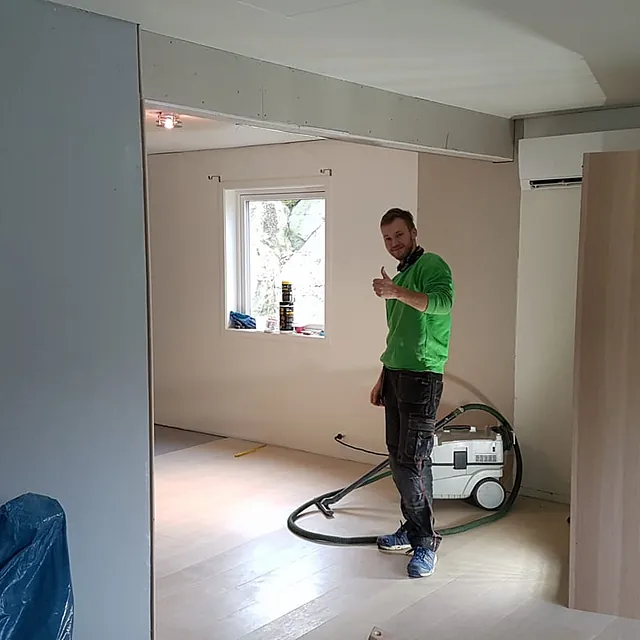 En ansatt som viser tommel opp i en nylig ferdig oppusset og utvidet lys stue