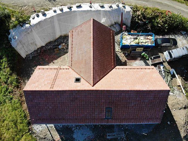 Drone bilde av et hus med et rødt tak, en cotainer fylt med skrot og blomsterbed som går rundt halve eiendommen