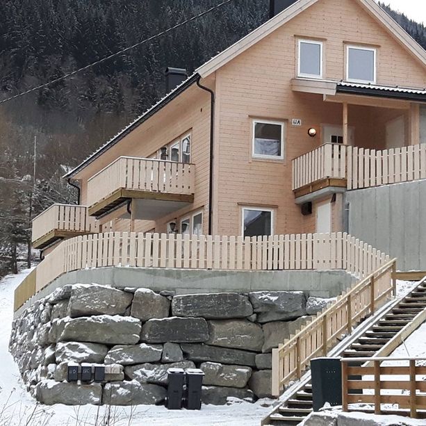 Ferdigstilt lyst hus med stein elementer som skiller ad forskjellige innganger til forskjellige etasjer med et fjell i bakgrunnen