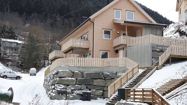 Ferdigstilt lyst hus med stein elementer som skiller ad forskjellige innganger til forskjellige etasjer med et fjell i bakgrunnen