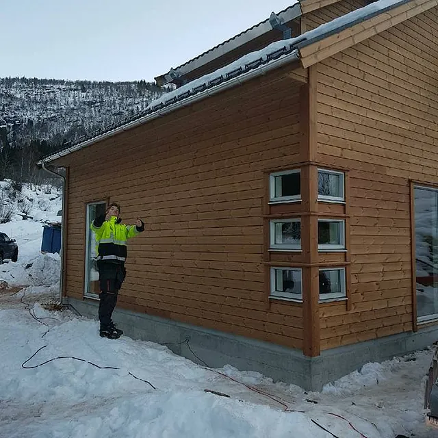 En ansatt som poserer fremfor et ferdig tilbygg med snø på bakken