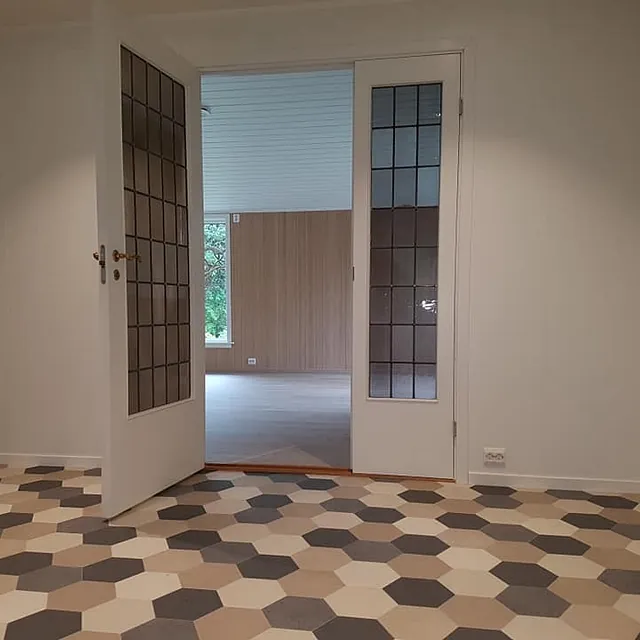 Retro glassdør som går fra et rom med geometriske fliser og inn til en lys stue med store vinduer