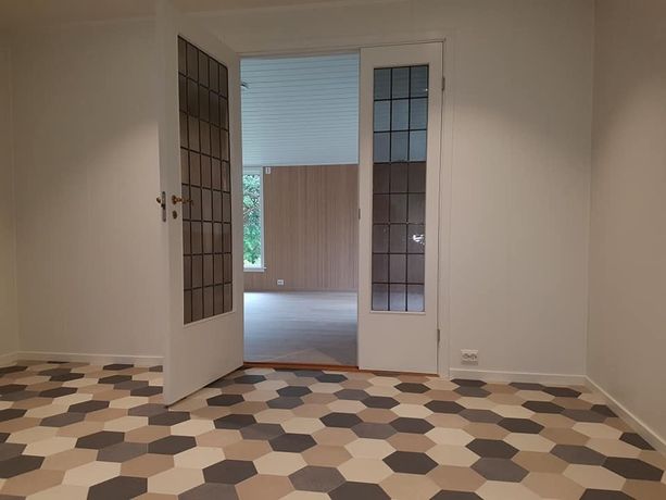 Retro glassdør som går fra et rom med geometriske fliser og inn til en lys stue med store vinduer