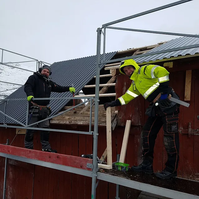 To ansatte som står på et stilas og bygger låvetak om vinteren