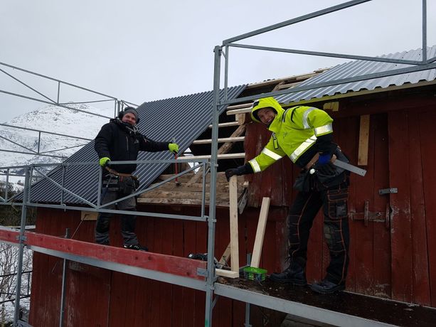 To ansatte som står på et stilas og bygger låvetak om vinteren